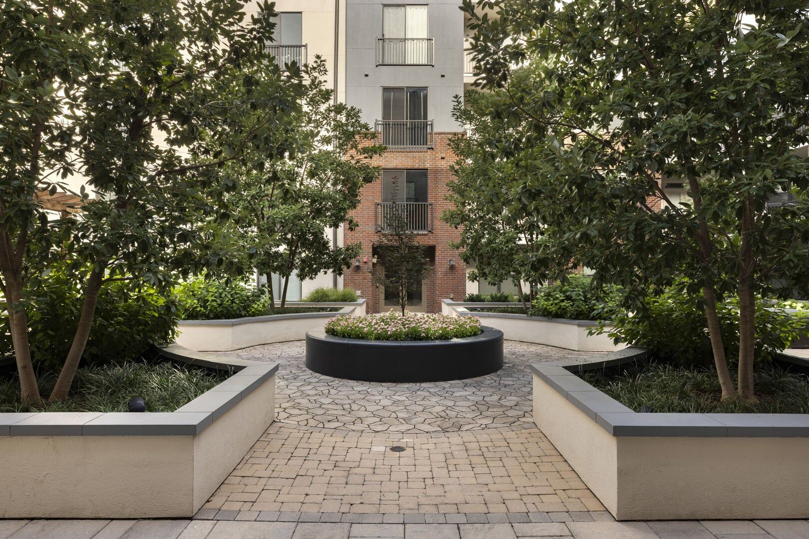 A courtyard with a central planter, surrounding brick walls, and trees.
