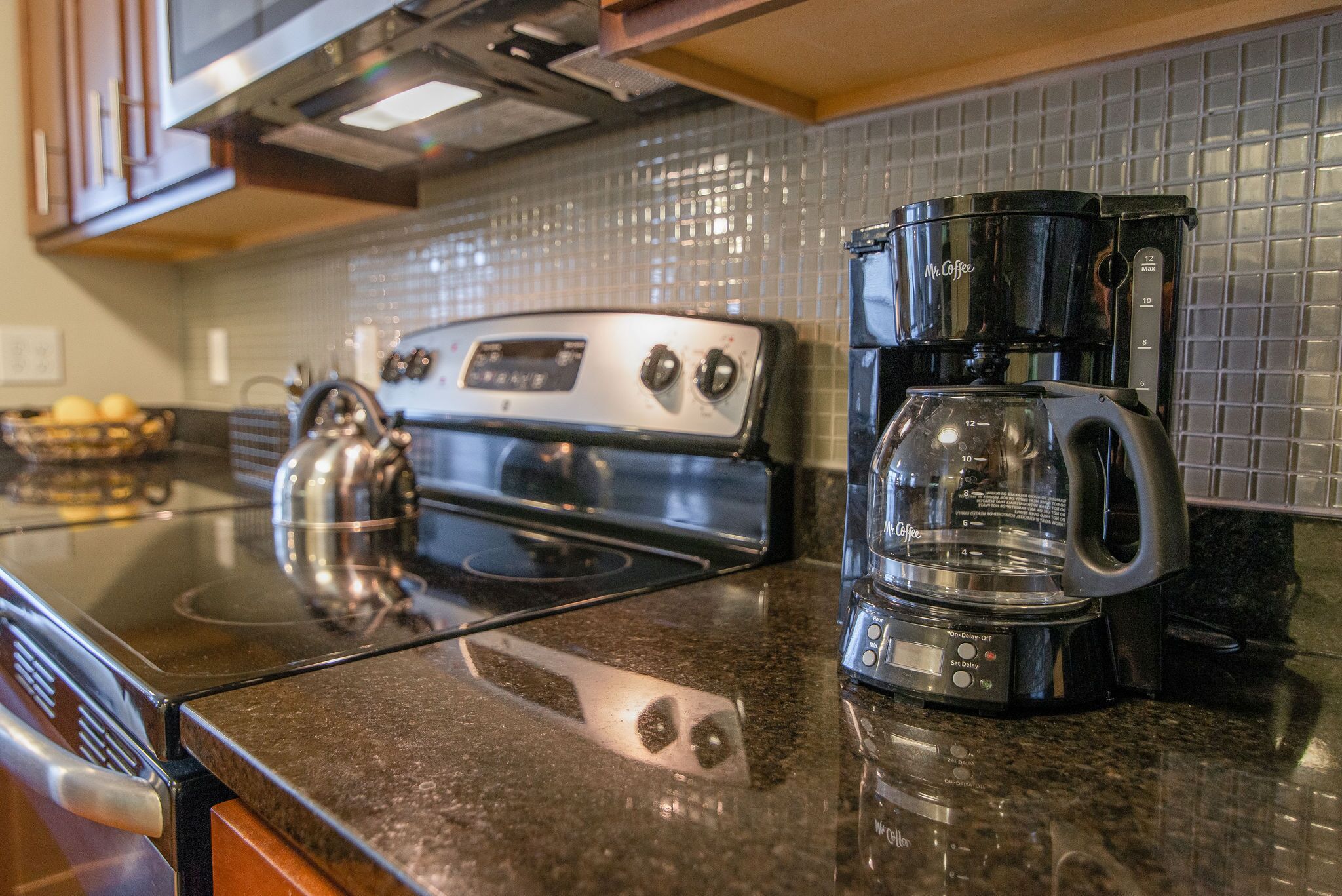 Una cocina con estufa negra, cafetera y salpicadero de azulejos.