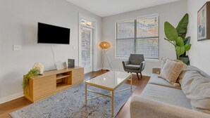 Un soggiorno moderno con televisore a schermo piatto, mobile TV in legno, tavolino in vetro, divano grigio e ampie finestre con persiane.