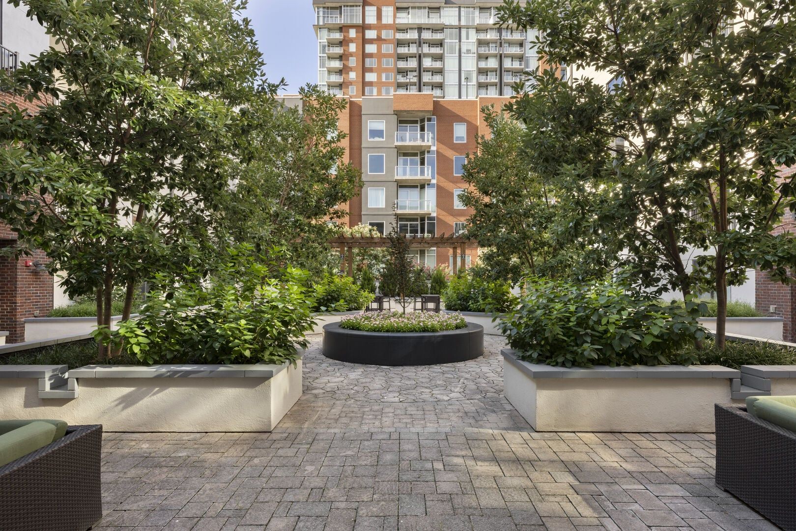 A courtyard with a central garden, surrounded by planters and seating areas, with a high-rise building in the background.