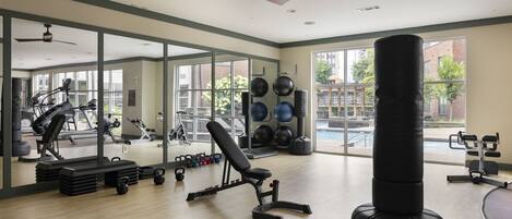 A gym with exercise equipment, a punching bag, and large windows offering a view of the outside.