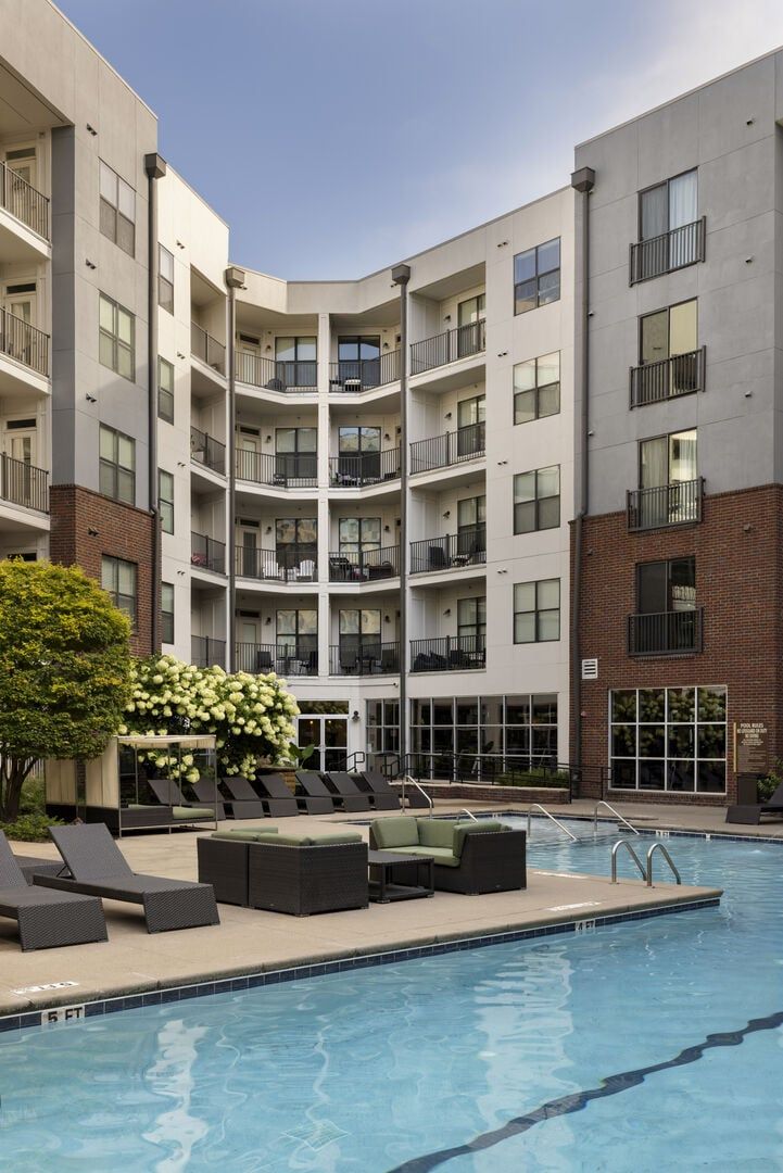 Un edificio residencial de varios pisos con balcones, piscina y mobiliario de exterior.
