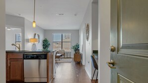 A modern kitchen with a dishwasher, a pendant light, and a dining area with a table and chairs. - Gulch Apartment with Gym 2BR/2BA (Nashville)