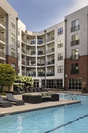 A multi-story residential building with balconies, a swimming pool, and outdoor seating.
