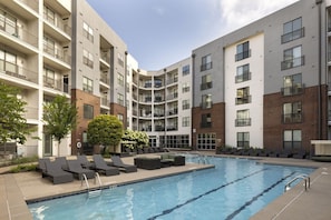 A multi-story residential building with a swimming pool, outdoor seating, and a brick facade.
