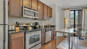 A modern kitchen with wooden cabinets, stainless steel appliances, and a dining area with a view of the city.