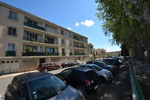 A row of parked cars along a street with a multi-story building featuring balconies with plants. - Charming Renovated Apartment Near the Historic Center of Tarascon (Tarascon)