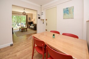 A dining area with a wooden table and red chairs, a sofa, and a painting on the wall.