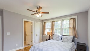 A bedroom with a bed, a nightstand, a lamp, a ceiling fan, and a window with curtains. - Charming Hillsboro Home Near Vanderbilt (Nashville)