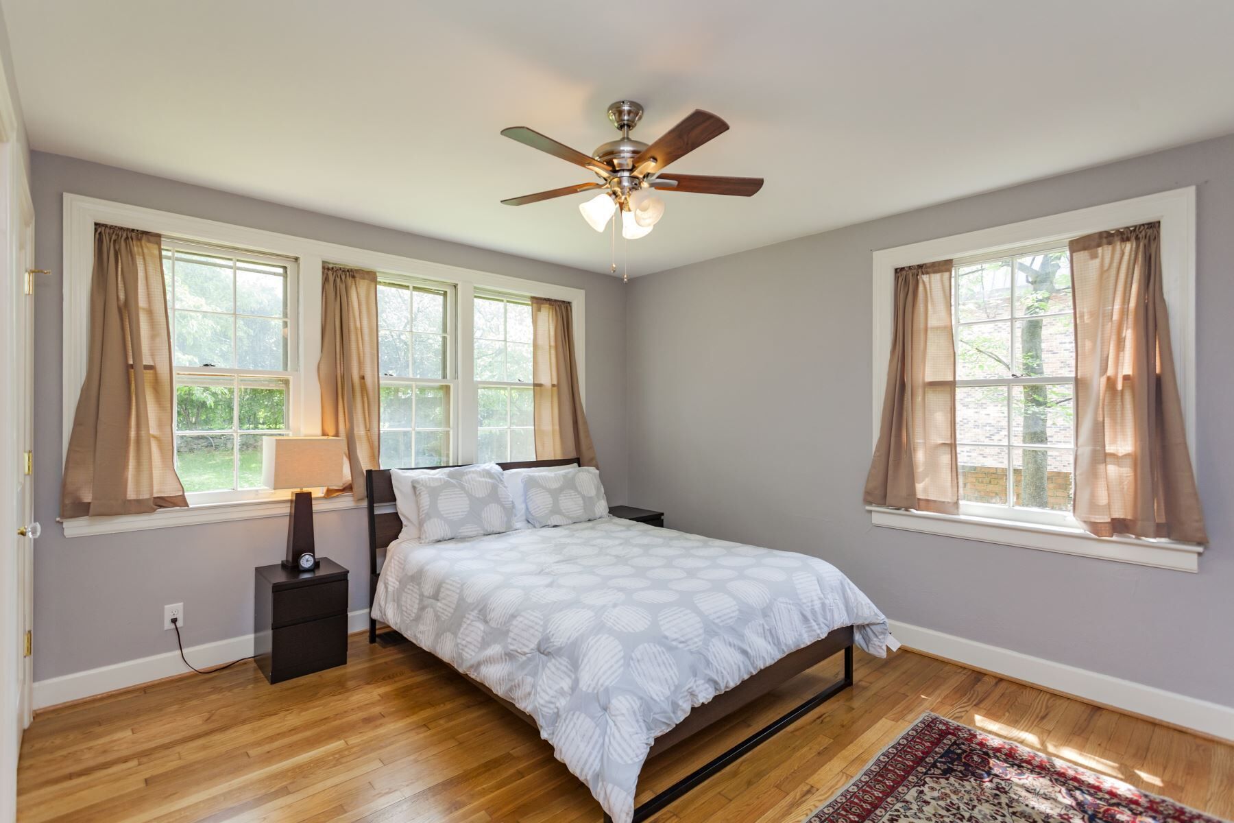 A bedroom with a bed, a ceiling fan, and two windows with curtains.