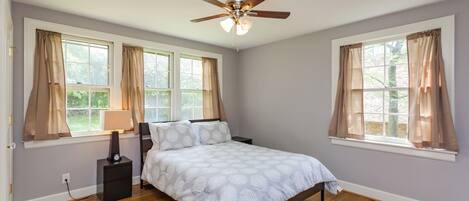 A bedroom with a bed, a ceiling fan, and two windows with curtains.