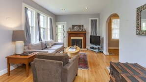 A spacious living room with a fireplace, a sofa, a television, and a wooden floor. - Charming Hillsboro Home Near Vanderbilt (Nashville)