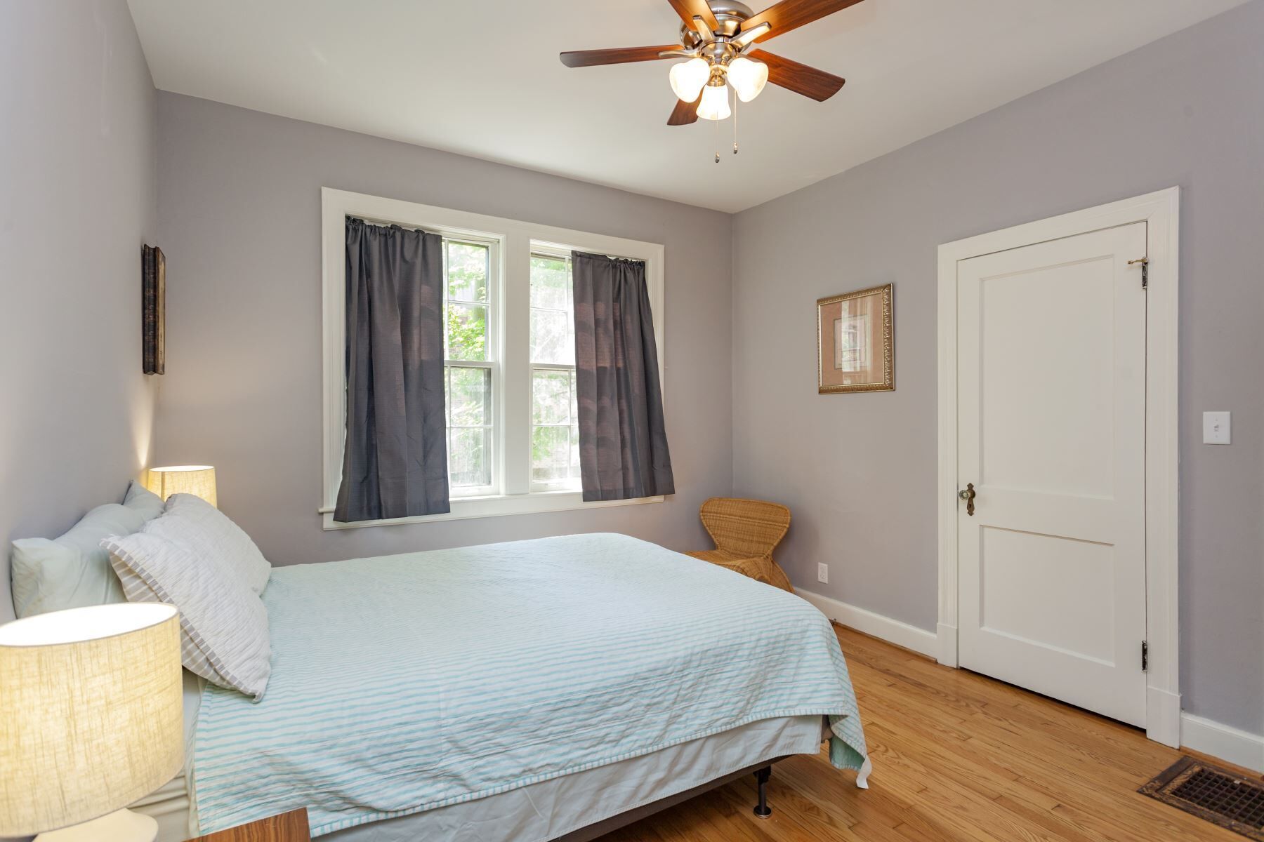 Une chambre à coucher avec un lit, une fenêtre avec des rideaux, un ventilateur de plafond et une porte.