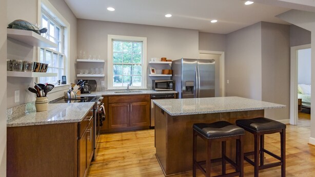 A modern kitchen with a large island, stainless steel appliances, wooden cabinets, and a window providing natural light. - Charming Hillsboro Home Near Vanderbilt (Nashville)