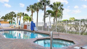 A swimming pool with a brick deck, surrounded by palm trees and a white fence.