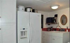 Compact kitchen with a refrigerator, microwave, sink, and mirror.