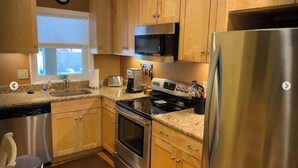 Una cocina con gabinetes de madera, electrodomésticos de acero inoxidable, microondas, estufa y refrigerador.