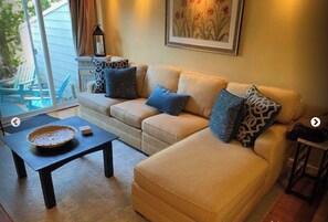 Relax in this inviting living room with a sofa, coffee table, and woven basket, offering a view of the serene outdoor space.