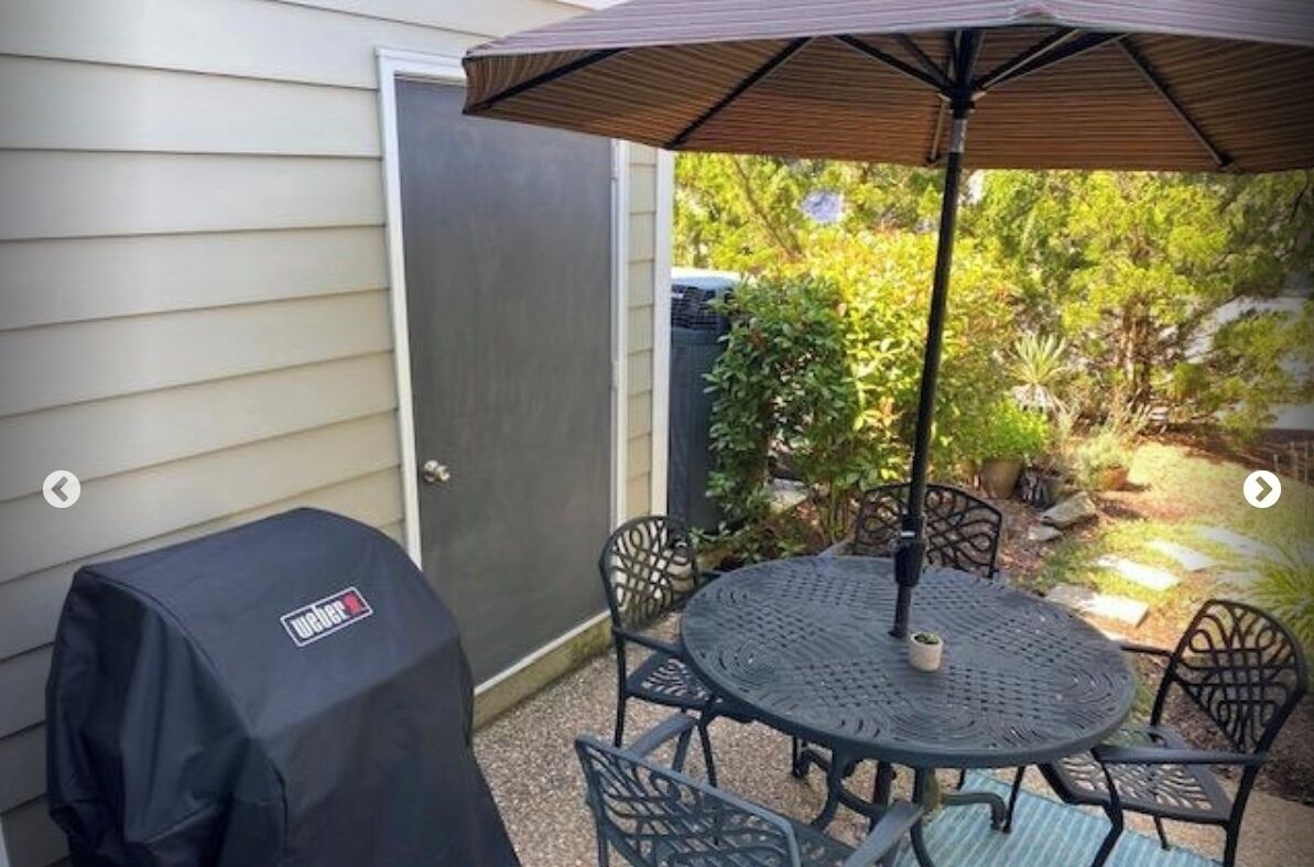 Une terrasse avec une table ronde et des chaises, un barbecue couvert et un parasol.