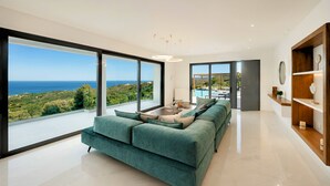 A modern living room with a large sofa, a coffee table, and a view of the sea. - Mistral Suite Heated Pool (Chania)