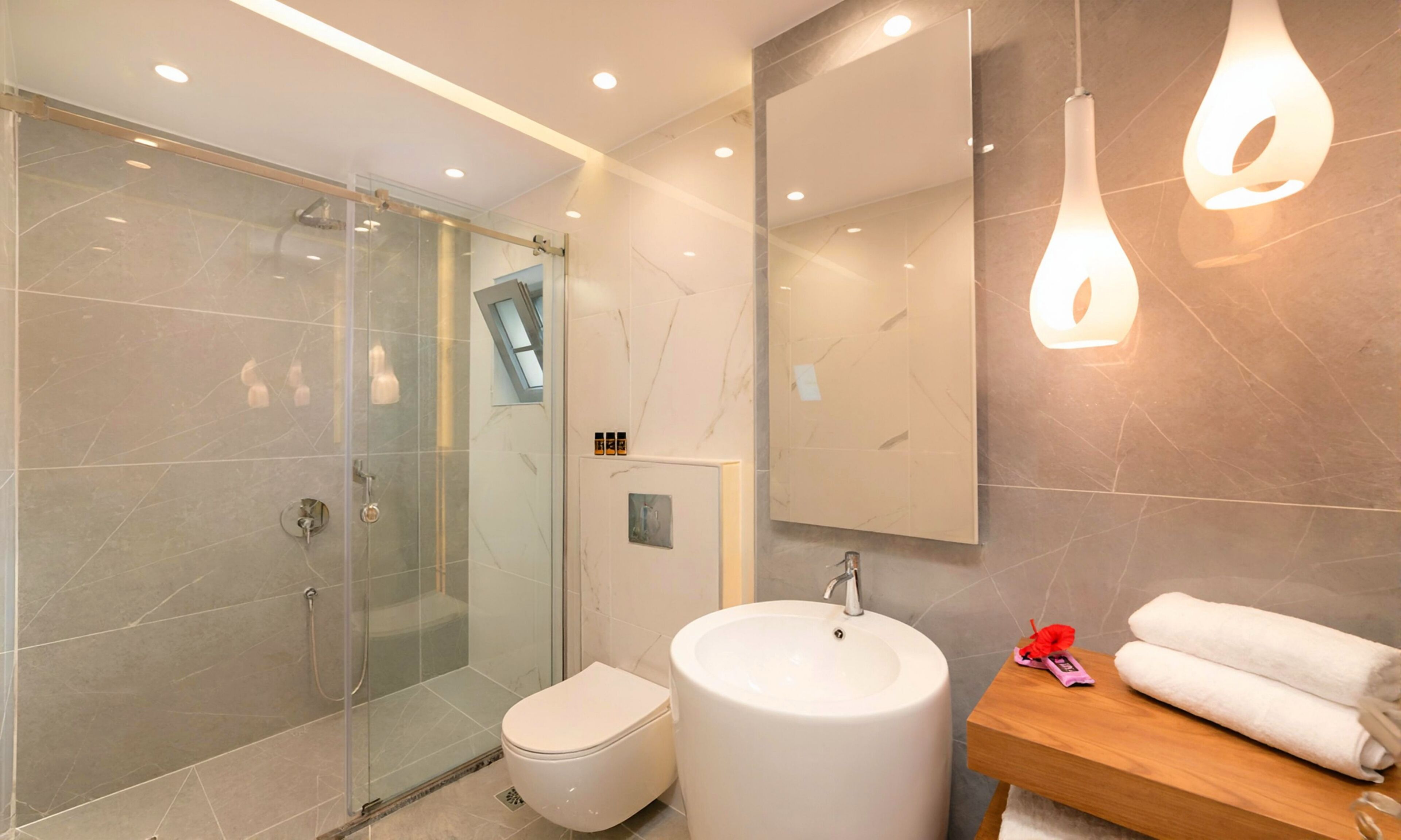 A modern bathroom with a glass-enclosed shower, a white toilet, a large sink, and a wooden vanity.