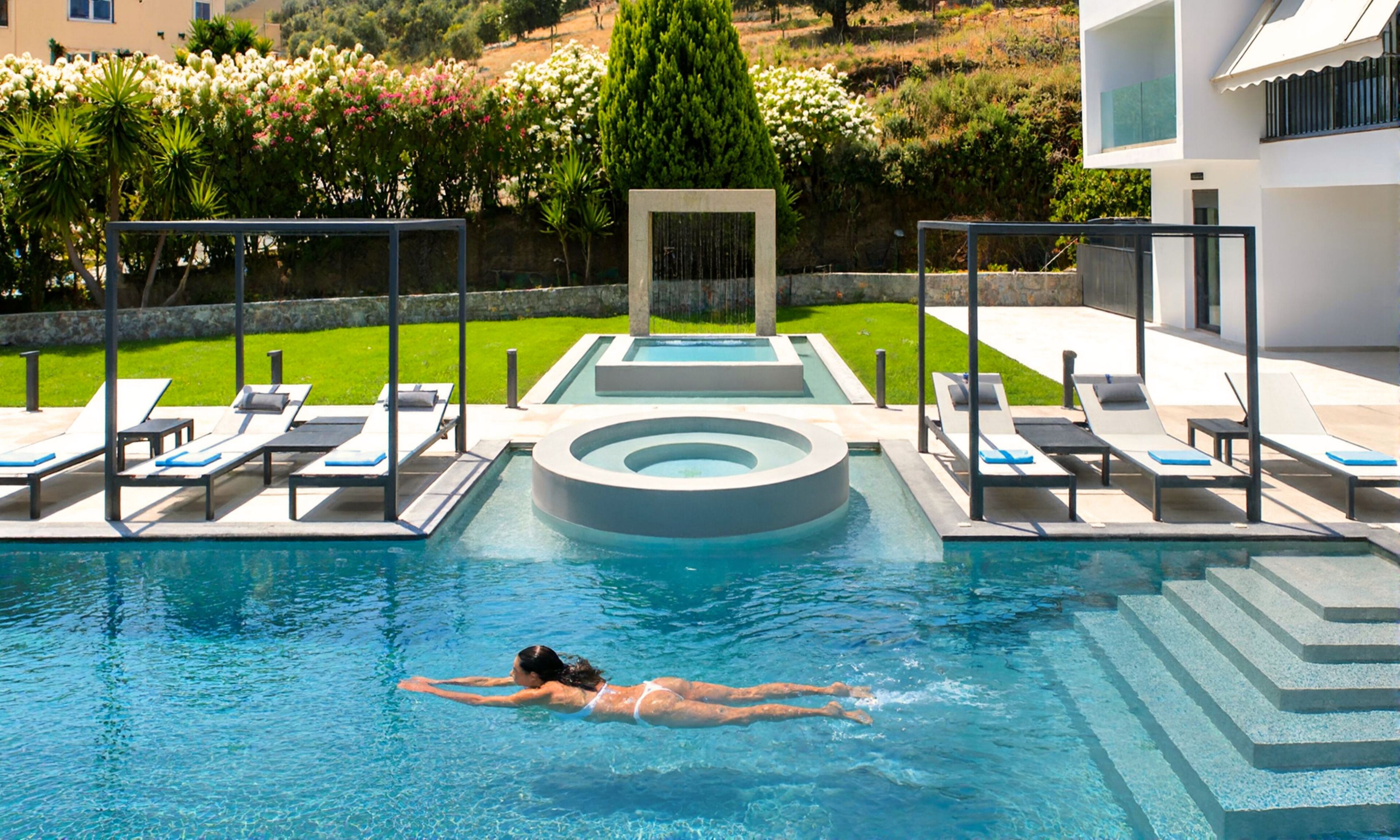 A swimming pool with a person swimming, lounge chairs, and a landscaped garden.