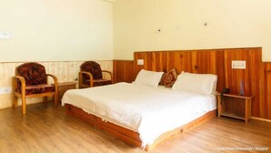 A single-bed room with a wooden headboard, two upholstered chairs, a bedside table with a lamp, and a wall-mounted light fixture. - Snow view Home Stay (Naggar)