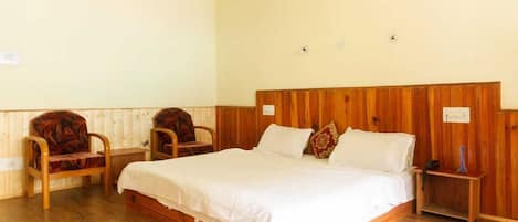A single-bed room with a wooden headboard, two upholstered chairs, a bedside table with a lamp, and a wall-mounted light fixture.