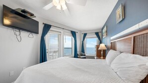 Ein Schlafzimmer mit einem großen Bett, einem Deckenventilator, einem an der Wand montierten Fernseher und Meerblick durch die Fenster.