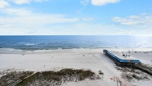 Ein Strand mit einer langen Mole, die ins Meer hinausführt, feinem Sand und einem wolkenlosen Himmel.