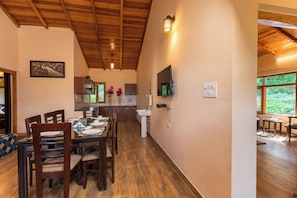 Un comedor con mesa y sillas de madera, una cocina con armarios y un lavamanos, y un ventanal con vistas a la vegetación.