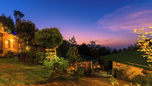 A rustic cottage with a dirt path leading to a wooden door, surrounded by lush greenery and a clear sky. - Oak Climbing Resort (Dhari)