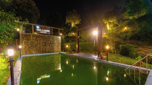A nighttime view of a swimming pool at Oak Climbing Resort, surrounded by well-lit pathways and greenery. - Oak Climbing Resort (Dhari)