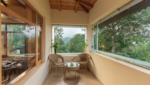 A cozy balcony with wicker chairs, a small round table, and a view of lush greenery and hills. - Oak Climbing Resort (Dhari)