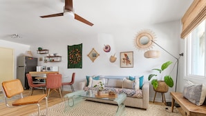 Un salon moderne avec une table basse en verre, un canapé, un coin repas avec des chaises et un ventilateur de plafond.