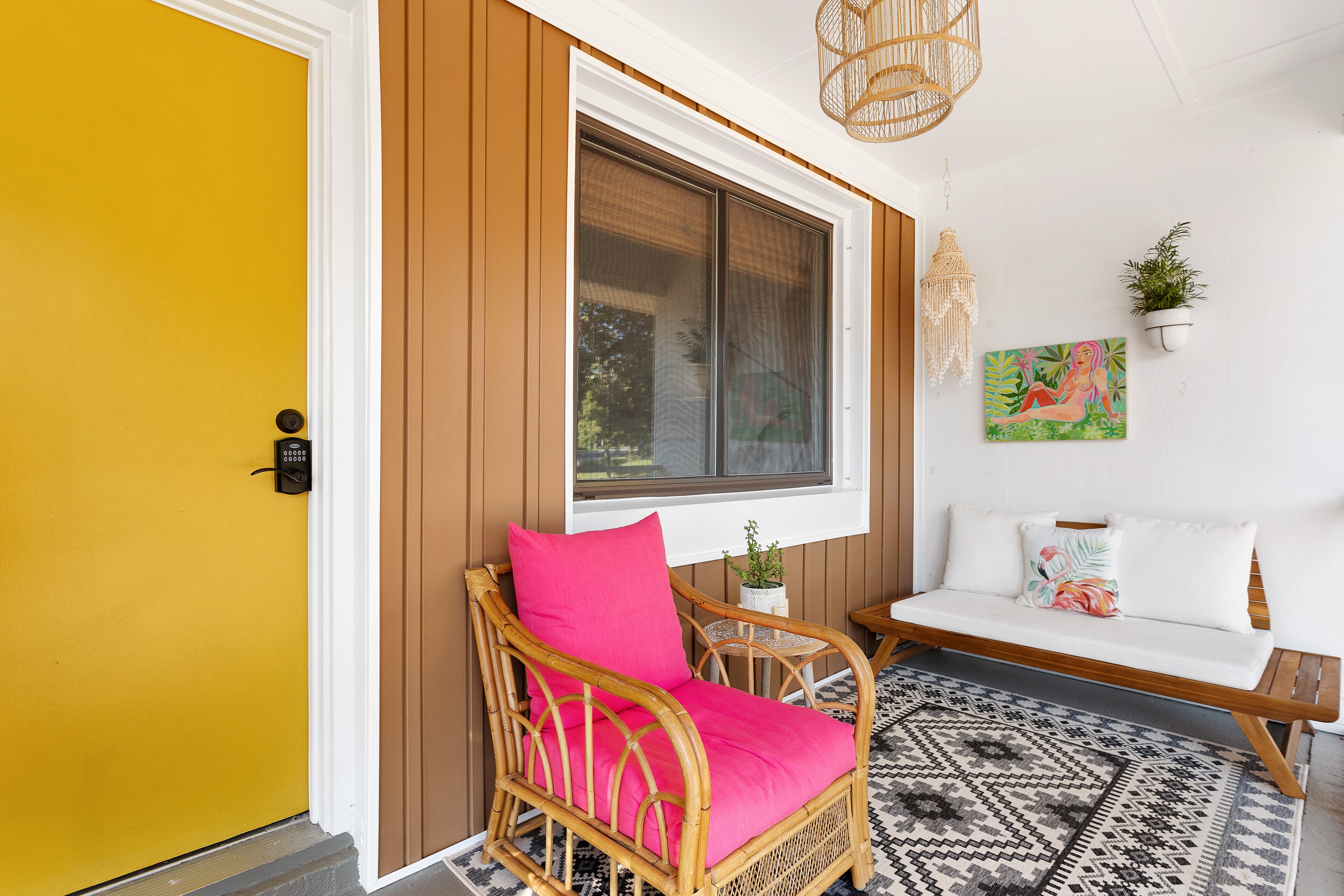 A wicker chair with a bright pink cushion, a white sofa, and a small table with a plant.