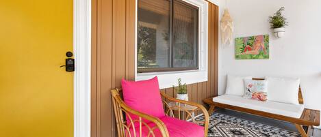 A wicker chair with a bright pink cushion, a white sofa, and a small table with a plant.