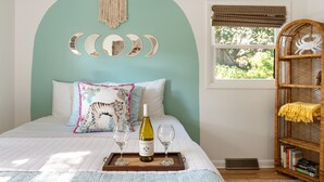 Une chambre à coucher avec un lit, une table de chevet sur laquelle se trouvent une bouteille de vin et des verres, une fenêtre donnant sur un paysage agréable et une bibliothèque.