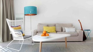 A modern living room with a white sofa, a white chair with colorful cushions, a round coffee table with oranges, and a blue lamp. - Villa 6 persons golf de la Palmyre, special offers for riders (Les Mathes)