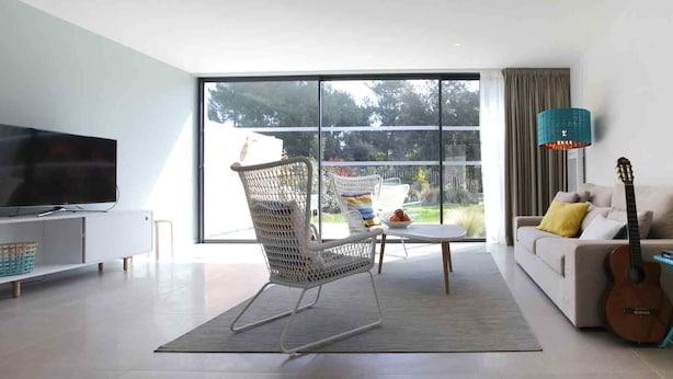 A modern living room with a TV, a white rocking chair, a sofa with cushions, a guitar, and a lamp. - Villa 6 persons golf de la Palmyre, special offers for riders (Les Mathes)