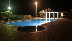 A swimming pool with a wooden deck, a covered pavilion, and a small hot tub.