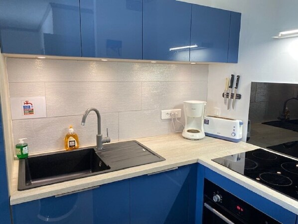 A modern kitchen with blue cabinets, a black sink, a coffee maker, and a toaster.