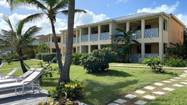 A resort building with multiple balconies, a pool area with lounge chairs, and a well-maintained lawn.