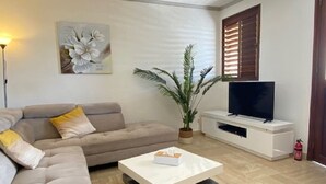 A modern living room with a sofa, a coffee table, a plant, a TV, and a fireplace.