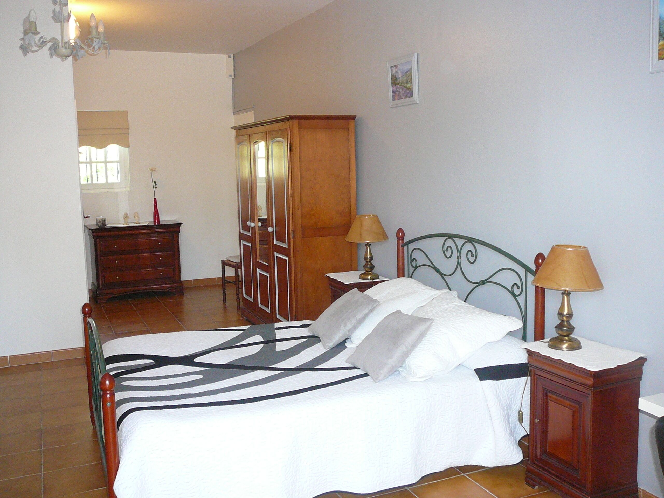 Een slaapkamer met een bed, twee nachtkastjes met lampen, een garderobe, een dressoir en een spiegel.