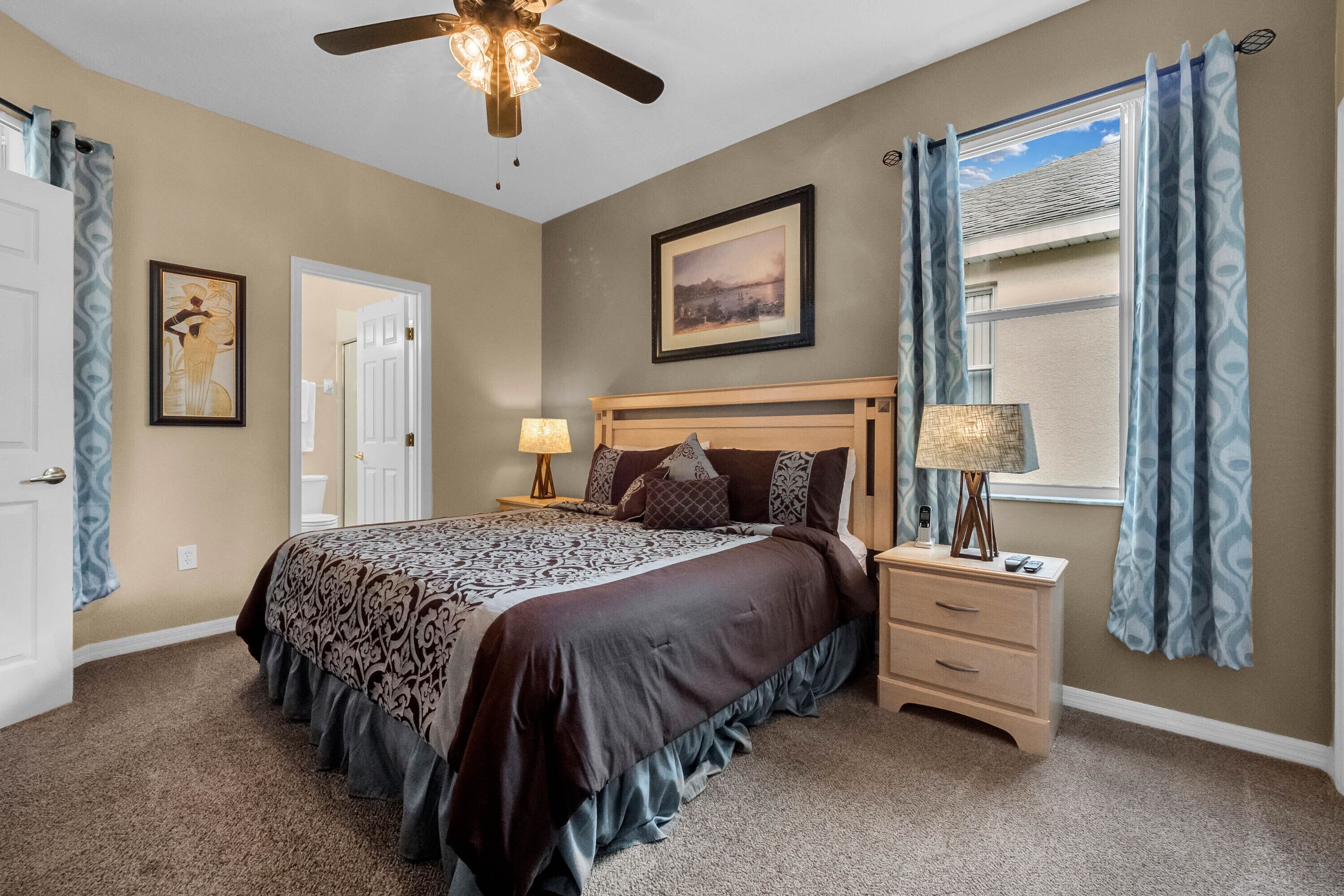 A bedroom with a bed, bedside table, lamp, and a ceiling fan.