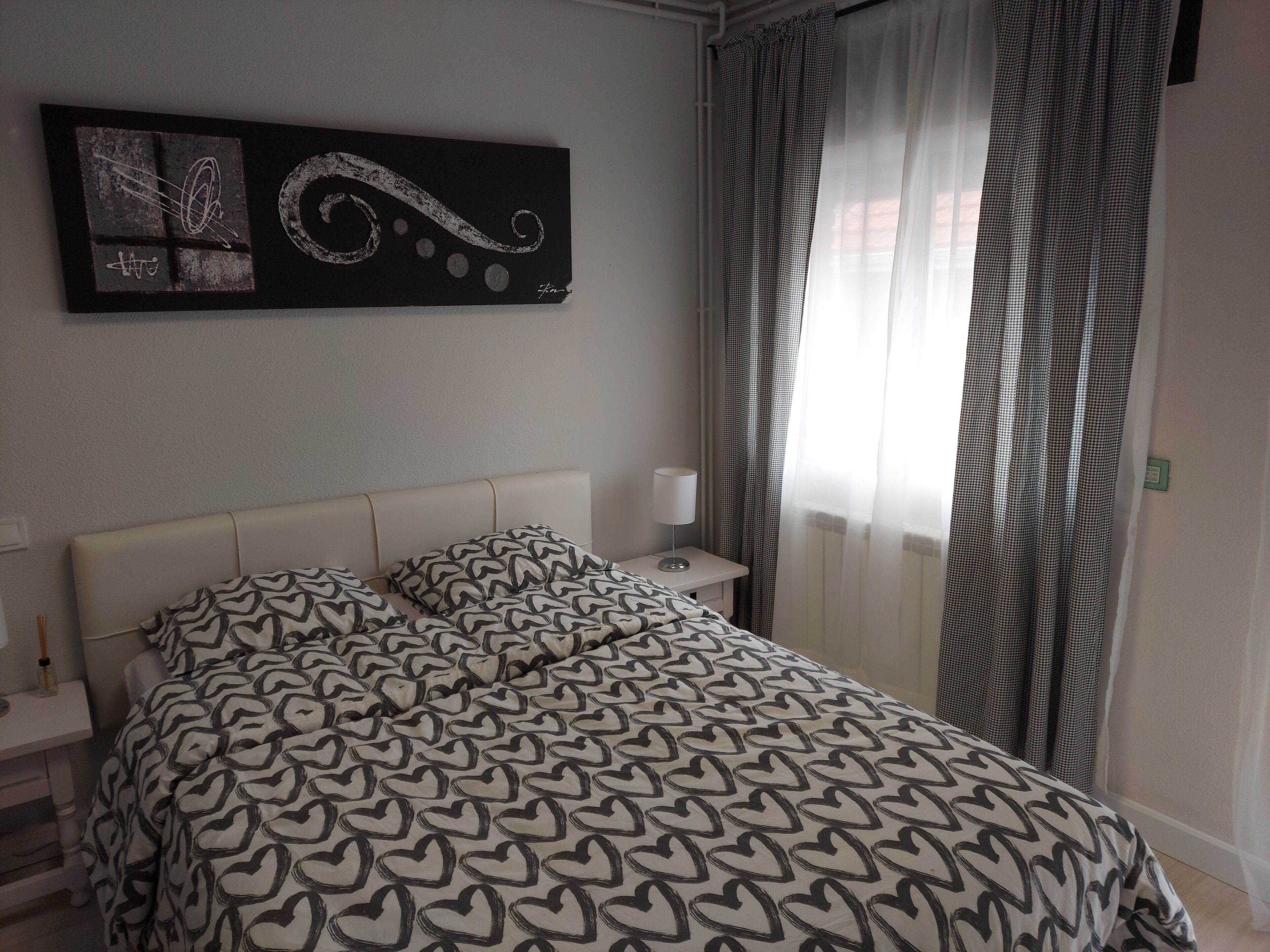 Una camera da letto con un letto, un comodino, una lampada, un quadro e una finestra con tende.