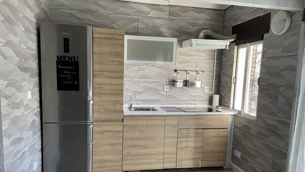 A compact kitchen with a built-in refrigerator, wooden cabinets, a microwave, and a window providing natural light. - navas suite (Navas del Rey)