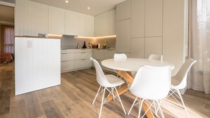 A modern kitchen with white cabinetry, a central island, and a round dining table with white chairs. - X-3 Ground floor apartment in community with pool (Calella de Palafrugell)