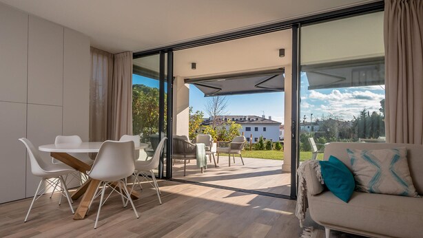 A modern living room with a dining area, large sliding glass doors leading to a patio, and a sofa with a throw pillow. - X-3 Ground floor apartment in community with pool (Calella de Palafrugell)